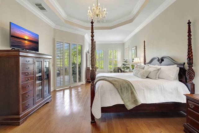 bedroom with visible vents, wood finished floors, an inviting chandelier, and a raised ceiling