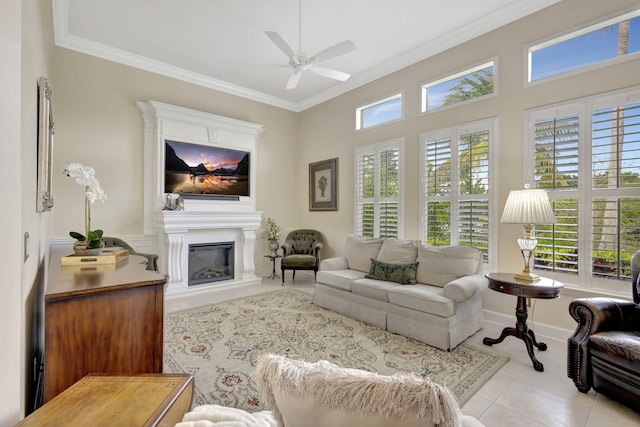living room with crown molding, baseboards, a ceiling fan, a glass covered fireplace, and tile patterned flooring