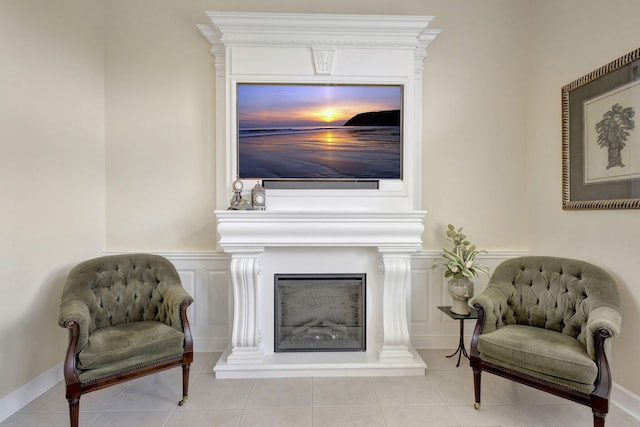 living area with a wainscoted wall, tile patterned floors, a fireplace with raised hearth, and a decorative wall