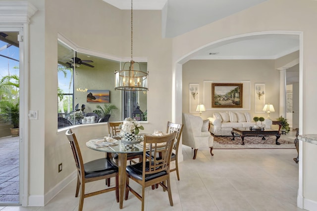 dining space featuring light tile patterned floors, ornamental molding, ceiling fan with notable chandelier, baseboards, and arched walkways