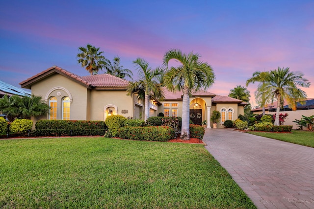 mediterranean / spanish-style house featuring a tile roof, stucco siding, an attached garage, decorative driveway, and a lawn