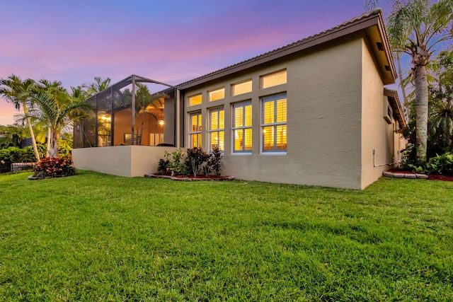 rear view of property featuring glass enclosure, a tile roof, a lawn, and stucco siding