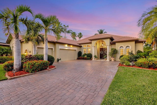 mediterranean / spanish house featuring decorative driveway, a tile roof, stucco siding, and a garage