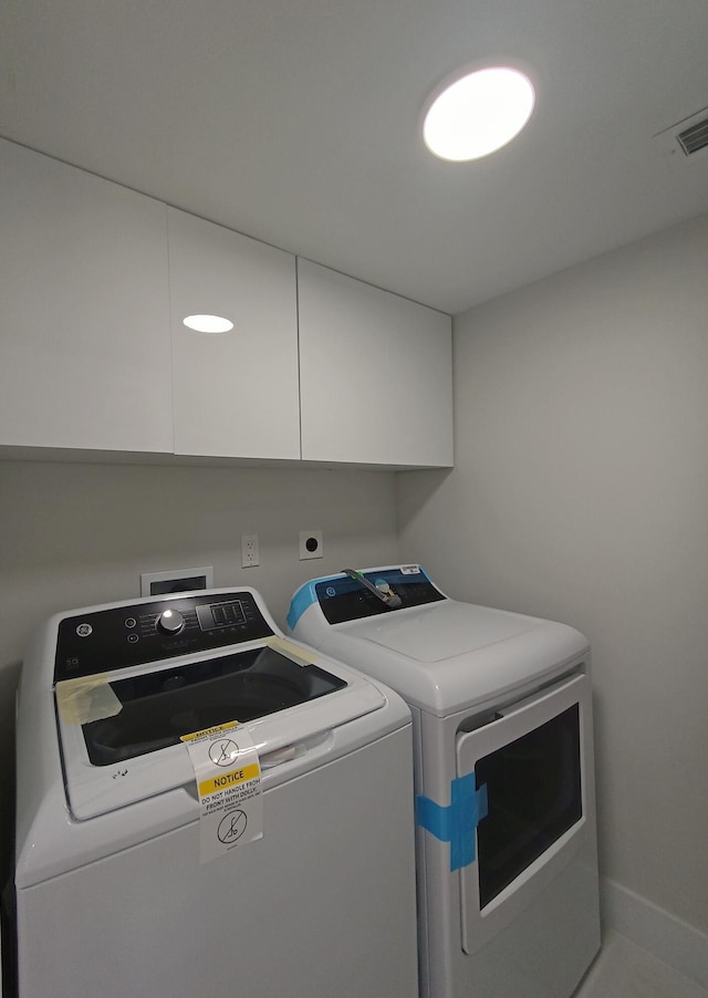 washroom with cabinet space, visible vents, and washer and clothes dryer