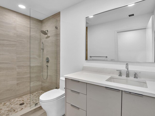 full bathroom with a tile shower, toilet, vanity, and recessed lighting