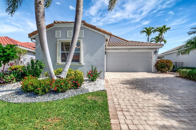 mediterranean / spanish house featuring a tiled roof, a garage, decorative driveway, and stucco siding