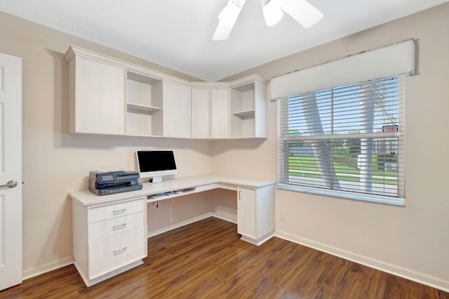 unfurnished office featuring built in desk, dark wood-style floors, baseboards, and ceiling fan