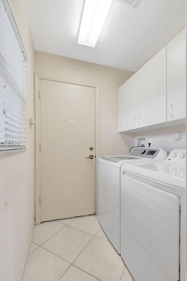 laundry room featuring washing machine and clothes dryer, cabinet space, light tile patterned floors, and a textured ceiling