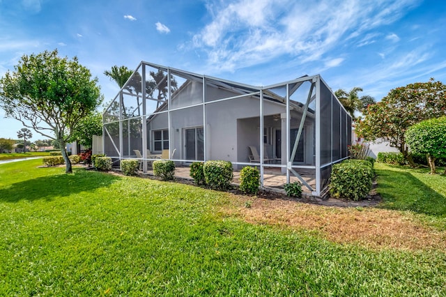 rear view of house with glass enclosure, stucco siding, and a yard