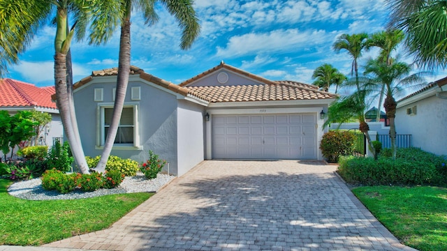 mediterranean / spanish-style house with decorative driveway, a tile roof, stucco siding, and a garage