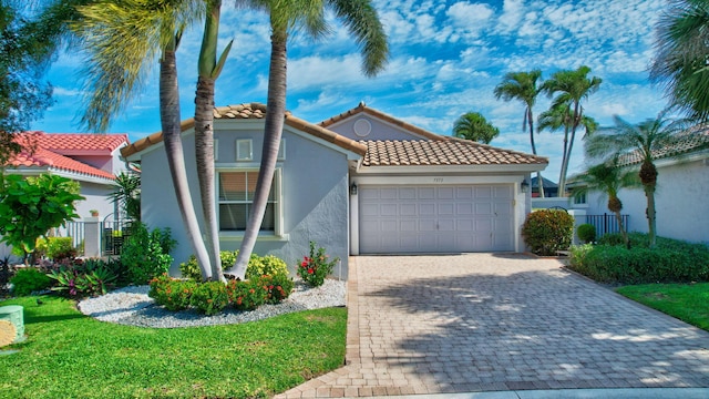 mediterranean / spanish home featuring a tile roof, stucco siding, fence, decorative driveway, and a garage