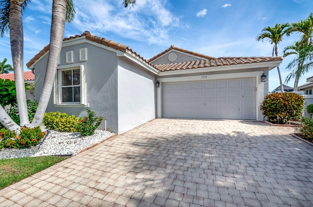 mediterranean / spanish home featuring stucco siding, a tile roof, a garage, and decorative driveway