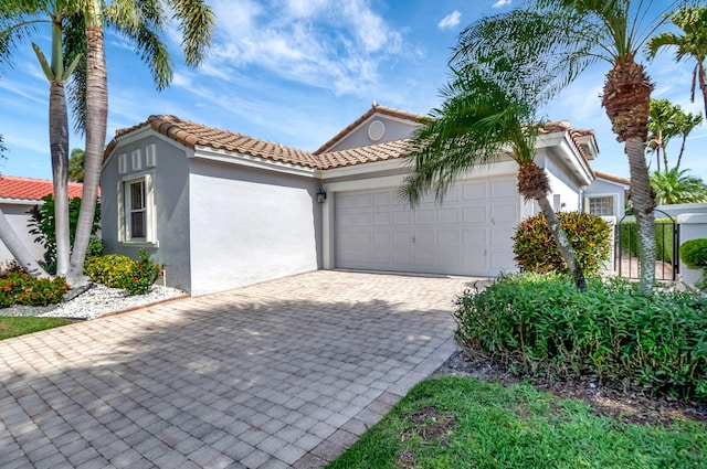 mediterranean / spanish home featuring decorative driveway, a tiled roof, stucco siding, and an attached garage