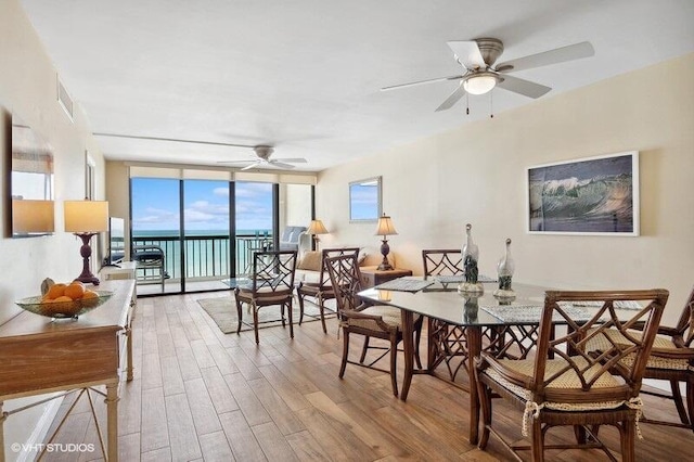 dining room with a wall of windows, visible vents, wood finished floors, and ceiling fan