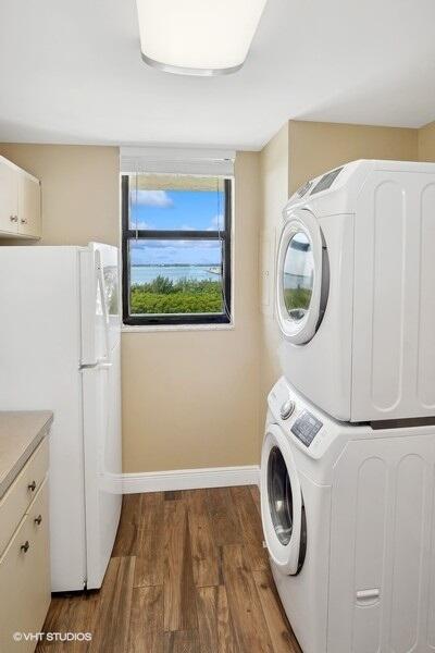 laundry area featuring stacked washer and dryer, baseboards, wood finished floors, and cabinet space