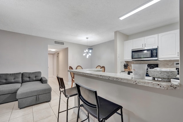 9441 W Mcnab Rd Unit 111, Tamarac, FL 33321 - kitchen with stainless steel microwave, white cabinets, decorative backsplash, a breakfast bar, and a textured ceiling