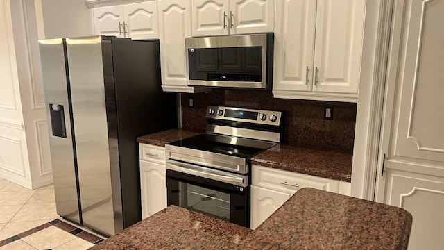 kitchen featuring white cabinets, tasteful backsplash, appliances with stainless steel finishes, dark stone countertops, and light tile patterned floors