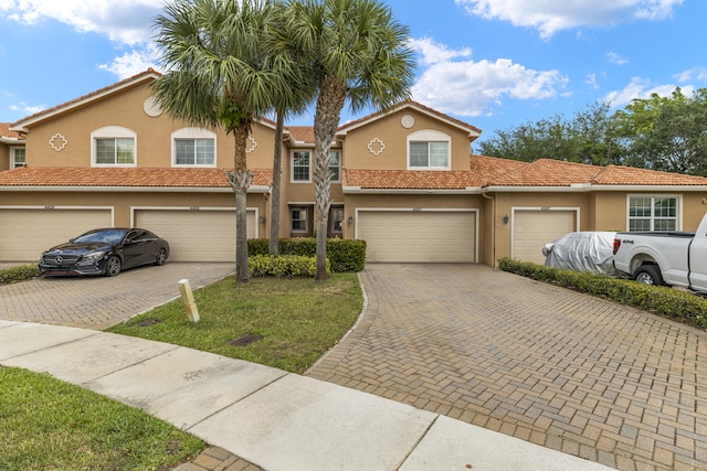 townhome / multi-family property featuring driveway, stucco siding, a garage, and a tile roof