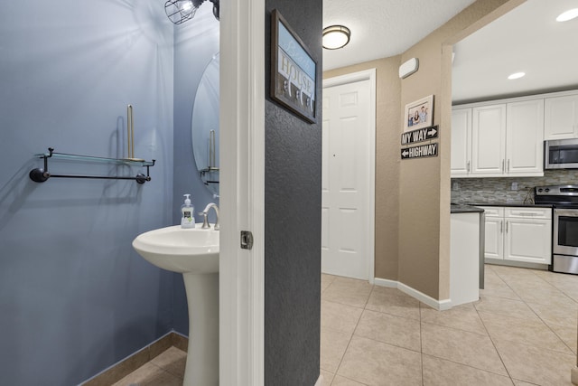 bathroom featuring tile patterned flooring, backsplash, baseboards, recessed lighting, and a sink