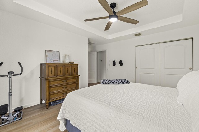 bedroom with a raised ceiling, a closet, light wood-style flooring, ceiling fan, and baseboards
