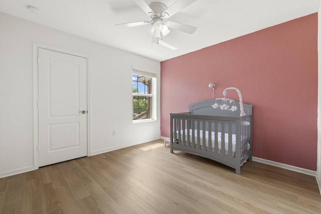 bedroom featuring wood finished floors, a crib, a ceiling fan, and baseboards