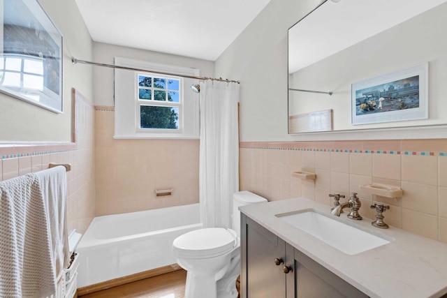 bathroom featuring tile walls, wainscoting, vanity, toilet, and shower / bath combo with shower curtain