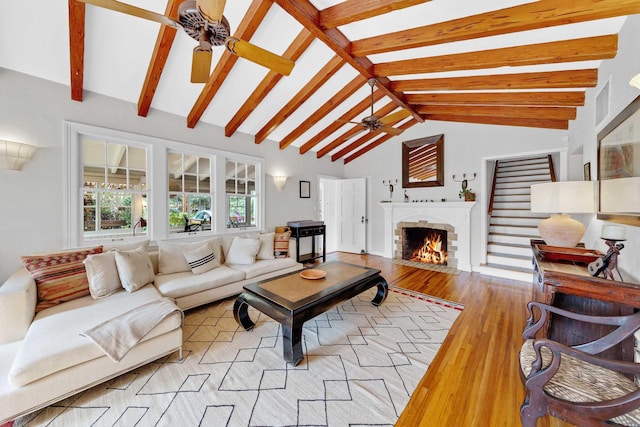 living room featuring light wood-type flooring, lofted ceiling with beams, a brick fireplace, and a ceiling fan