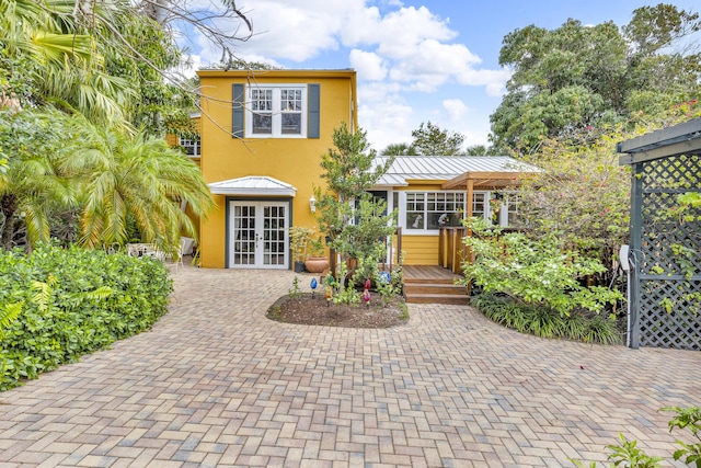 view of front of property featuring french doors, metal roof, a deck, decorative driveway, and stucco siding