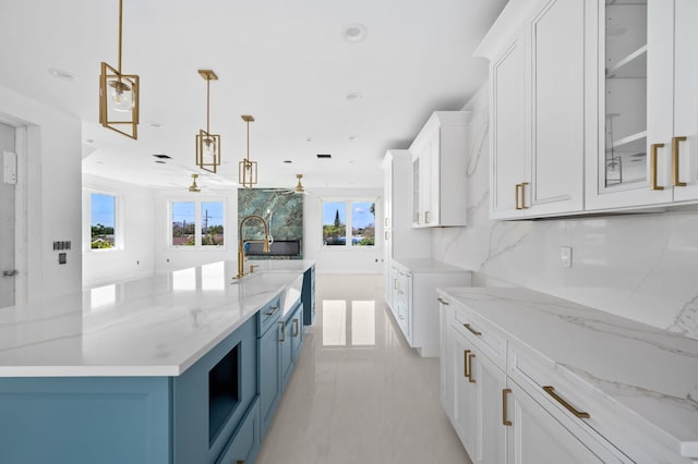 kitchen with light stone counters, blue cabinets, white cabinetry, and ceiling fan