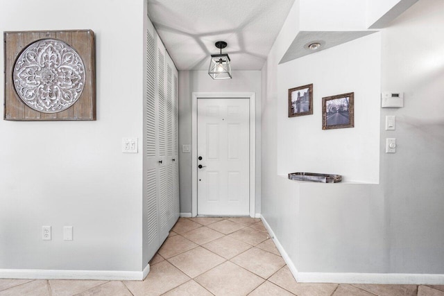 hall featuring light tile patterned floors, baseboards, and a textured ceiling