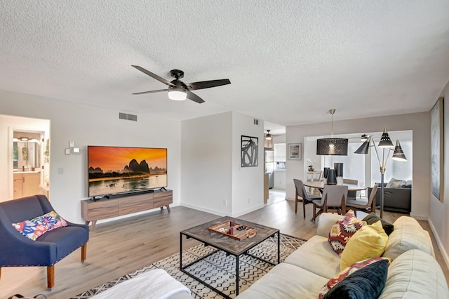 living room featuring wood finished floors, a textured ceiling, ceiling fan, and visible vents