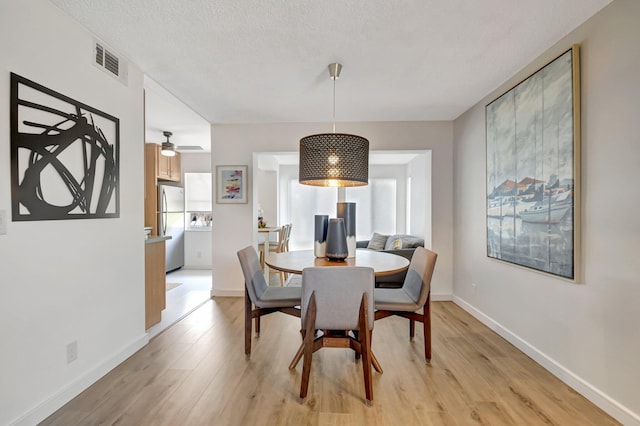 dining area with a textured ceiling, visible vents, baseboards, a ceiling fan, and light wood-style floors
