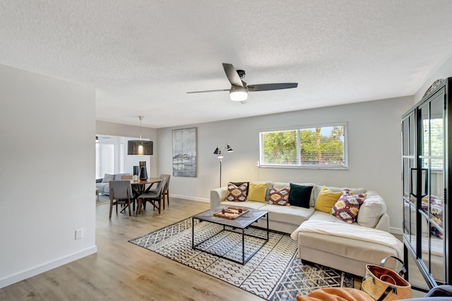 living area with baseboards, a textured ceiling, ceiling fan, and wood finished floors