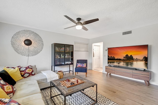 living room featuring visible vents, wood finished floors, ceiling fan, and a textured ceiling