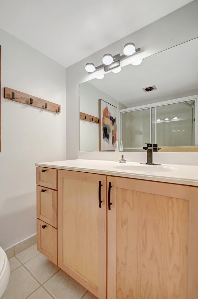 bathroom with a stall shower, tile patterned floors, toilet, vanity, and baseboards