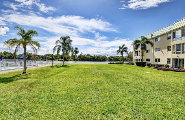 view of property's community with a lawn, a water view, fence, and a swimming pool