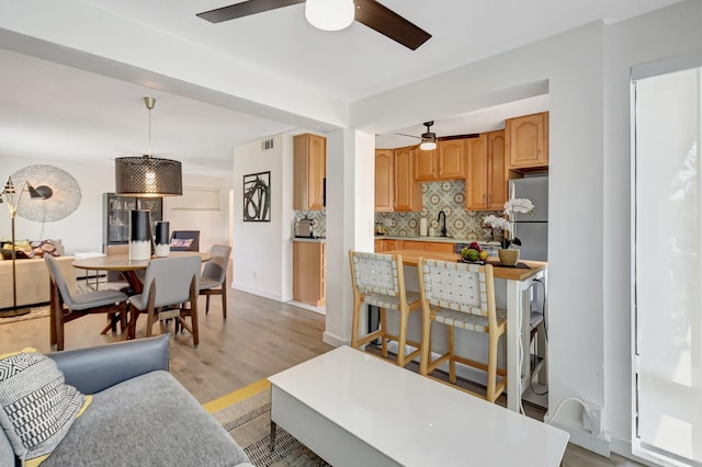 living area featuring baseboards, visible vents, light wood-style flooring, and a ceiling fan
