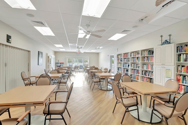 dining space with light wood-type flooring, a drop ceiling, ceiling fan, and visible vents