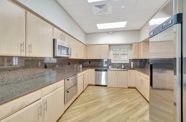 kitchen featuring dark stone counters, stainless steel appliances, and light brown cabinetry