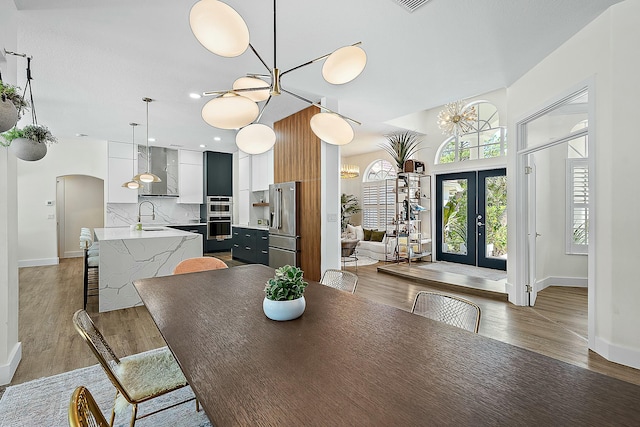 dining room with light wood-type flooring, baseboards, a chandelier, french doors, and arched walkways