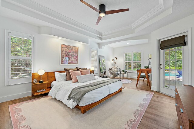 bedroom featuring crown molding, a raised ceiling, access to outside, light wood-style floors, and ceiling fan