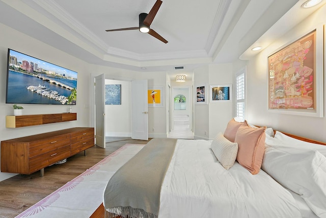 bedroom featuring a raised ceiling, ornamental molding, wood finished floors, ensuite bath, and baseboards