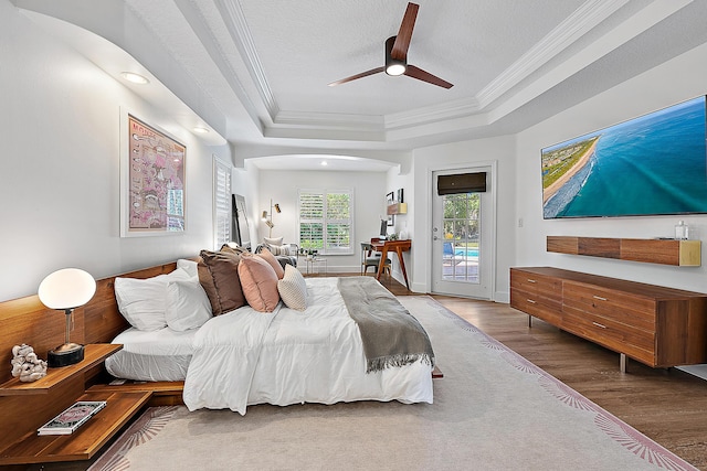 bedroom with access to outside, crown molding, a raised ceiling, wood finished floors, and a ceiling fan