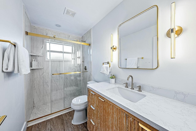 full bathroom featuring toilet, a marble finish shower, wood finished floors, and vanity