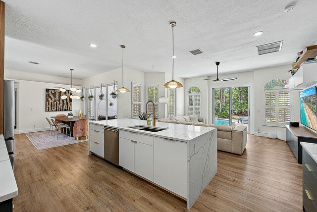 kitchen with a sink, appliances with stainless steel finishes, light wood finished floors, open floor plan, and an island with sink