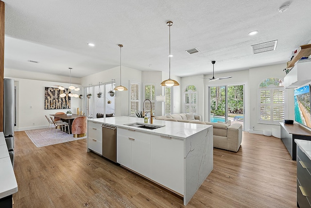 15415 Alexander Run, Jupiter, FL 33478 - kitchen featuring a sink, dishwasher, light wood finished floors, a textured ceiling, and a center island with sink