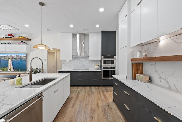 kitchen featuring stainless steel appliances, a sink, wall chimney exhaust hood, modern cabinets, and dark cabinets