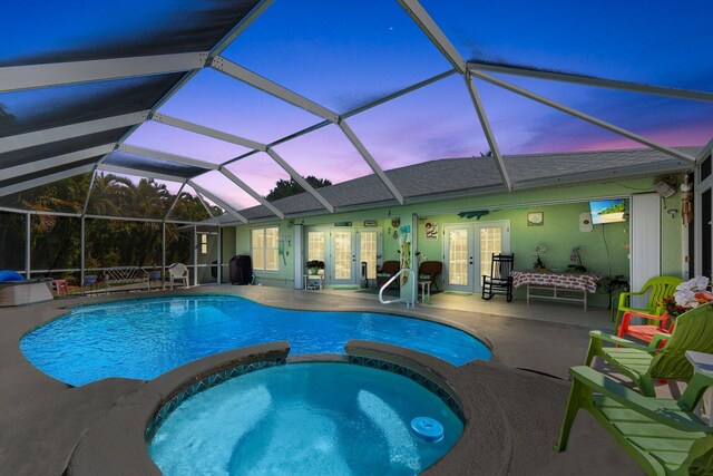 pool at dusk featuring french doors, a pool with connected hot tub, glass enclosure, and a patio area