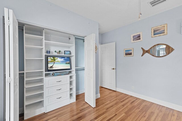 bedroom with baseboards, visible vents, light wood finished floors, and a closet