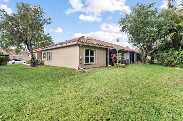 back of house featuring a tile roof, a lawn, and stucco siding